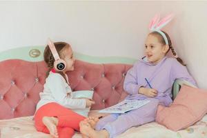 duas irmãs se divertem em casa, desenham um coelho e ouvem música em fones de ouvido, a mais velha tem uma faixa de cabelo com orelhas de coelho na cabeça, esperando o feriado da páscoa foto