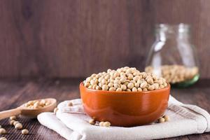 cru soja sementes dentro uma tigela, colher e jarra em a mesa. fonte do vegetal proteína. foto