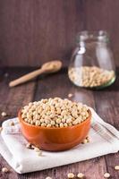 cru soja sementes dentro uma tigela, colher e jarra em a mesa. fonte do vegetal proteína. vertical Visão foto