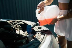 jovem mulher derramando líquido de lavagem de tela de carro anticongelante no carro foto