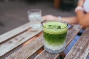 chá com leite matcha verde gelado na mesa de madeira foto