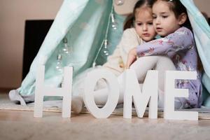 dois meninas irmãs às wigwam barraca com de madeira casa cartas. foto