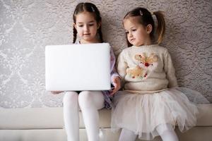 dois meninas irmãs assistindo em computador portátil. tecnologia e casa conceito. foto