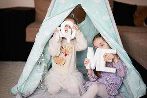 dois meninas irmãs às wigwam barraca com de madeira casa cartas. foto