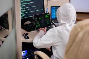 Garoto hacker fraudulentamente usar crédito cartão para pagamento. Internet roubo . homem vestindo uma balaclava e segurando uma crédito cartão enquanto Sentou atrás uma computador portátil. foto