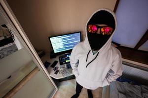 Garoto hacker. Internet roubo . homem vestindo uma balaclava atrás uma computador portátil. foto