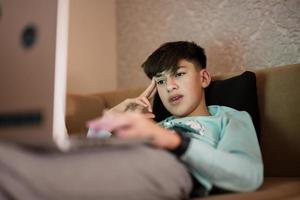 jovem adolescente Garoto dentro frente do uma computador portátil em uma cama às tarde. foto