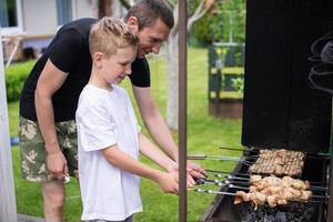 alegre Papai e filho assado carne em a grade foto