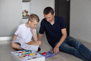 uma fofa Garoto dentro uma branco camiseta coleta a elétrico desenhador com dele Papai dentro a quarto foto