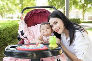 lindo mãe com uma bebê menina sentado em bebê carrinho ao ar livre dentro brilho do sol dia foto