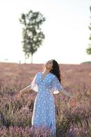 retrato do uma feliz mulher dentro uma azul vestir desfrutando uma ensolarado verão dia dentro uma lavanda campo. fresco ar, estilo de vida. foto