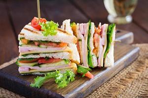 clube sanduíche com presunto, tomate, pepino, queijo, e Rúcula em de madeira fundo. foto