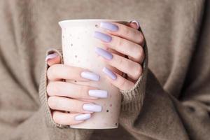 as mãos da menina com delicada manicure roxa segurando uma xícara de chá. foto