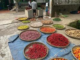 vários legumes tomates, Pimenta, vermelho cebola, milho, cenoura, Lima, alho ser vendido às ásia tradicional mercado. colorida legumes em volta bambu bandeja às tradicional mercado chão foto