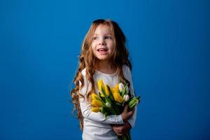 retrato do uma encantador sorridente pequeno menina com uma ramalhete do tulipas dentro dela mãos. estilo de vida. fresco flores internacional mulheres dia. espaço para texto. Alto qualidade foto