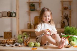 fofa pequeno menina come natural pastilha às casa dentro uma de madeira cozinha. Comida para crianças a partir de natural produtos foto