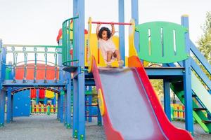 moreno bebê com encaracolado cabelo dentro uma pálido Rosa vestir tocam em uma rua Parque infantil e passeios baixa a colina. a conceito do uma saudável estilo de vida. feliz infância. Alto qualidade foto