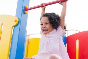 moreno bebê com encaracolado cabelo dentro uma pálido Rosa vestir tocam em uma rua Parque infantil e passeios baixa a colina. a conceito do uma saudável estilo de vida. feliz infância. Alto qualidade foto