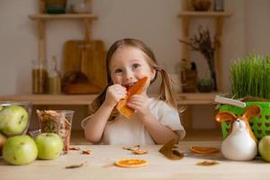 fofa pequeno menina come natural pastilha às casa dentro uma de madeira cozinha. Comida para crianças a partir de natural produtos foto