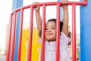 moreno bebê com encaracolado cabelo dentro uma pálido Rosa vestir tocam em uma rua Parque infantil e passeios baixa a colina. a conceito do uma saudável estilo de vida. feliz infância. Alto qualidade foto