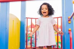 moreno bebê com encaracolado cabelo dentro uma pálido Rosa vestir tocam em uma rua Parque infantil e passeios baixa a colina. a conceito do uma saudável estilo de vida. feliz infância. Alto qualidade foto