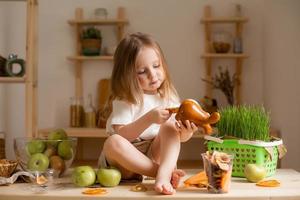 fofa pequeno menina come natural pastilha às casa dentro uma de madeira cozinha. Comida para crianças a partir de natural produtos foto