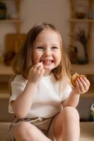 fofa pequeno menina come natural pastilha às casa dentro uma de madeira cozinha. Comida para crianças a partir de natural produtos foto