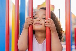 moreno bebê com encaracolado cabelo dentro uma pálido Rosa vestir tocam em uma rua Parque infantil e passeios baixa a colina. a conceito do uma saudável estilo de vida. feliz infância. Alto qualidade foto