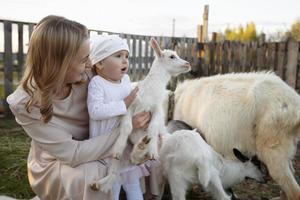 mãe com uma pequeno filha feeds uma cabra. uma mulher com uma criança em uma Fazenda. foto