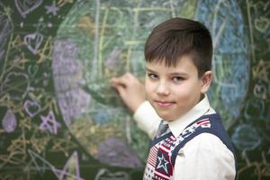 a estudante às a quadro-negro desenha com giz. meio escola idade. a Garoto é dentro a sala de aula. foto