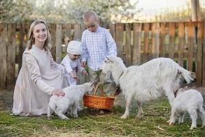 mãe com uma pequeno filha feeds uma cabra. mulher com crianças em a Fazenda. família com cabras. Vila vida. foto