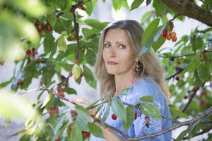 uma lindo idosos mulher colheitas dentro a país. uma cinquenta anos mulher dentro a galhos do uma cereja fruta árvore. foto