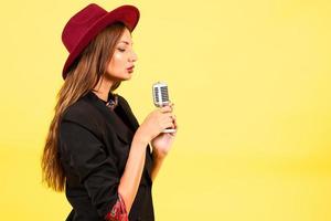 menina dentro uma Preto terno em uma amarelo fundo canta dentro uma retro microfone, retrato, música foto