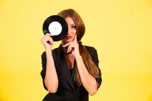 menina dentro uma Preto terno em uma amarelo fundo com uma registro dentro dela mãos, música, a menina mostra emoções foto