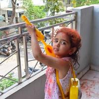 doce pequeno indiano menina jogando cores em holi festival, segurando pichakaree cheio do cores, holi festival celebrações dentro Délhi, Índia foto