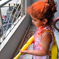 doce pequeno indiano menina jogando cores em holi festival, segurando pichakaree cheio do cores, holi festival celebrações dentro Délhi, Índia foto