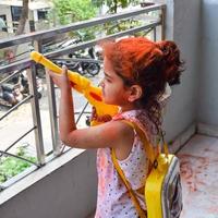 doce pequeno indiano menina jogando cores em holi festival, segurando pichakaree cheio do cores, holi festival celebrações dentro Délhi, Índia foto