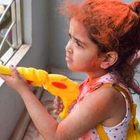 doce pequeno indiano menina jogando cores em holi festival, segurando pichakaree cheio do cores, holi festival celebrações dentro Délhi, Índia foto