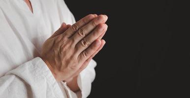 um adulto cuja mão é rezada no fundo escuro.respeito pela crença na religião e em deus. vista frontal. conceito de paz. foto