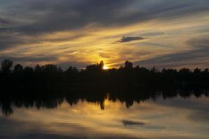 infernal pôr do sol atrás árvores e reflexão dentro água. foto