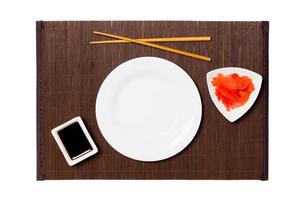 prato branco redondo vazio com pauzinhos para sushi, gengibre e molho de soja no fundo escuro da esteira de bambu. vista superior com espaço de cópia para você projetar foto