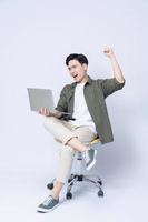 jovem ásia o negócio homem sentado em cadeira e usando computador portátil em fundo foto