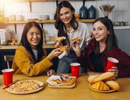 jovem mulher comendo pizza e rindo enquanto sentado com dela amigos dentro uma restaurante. grupo do amigos desfrutando enquanto tendo Comida e bebidas às cafeteria. foto