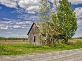 um celeiro abandonado próximo a árvores em um campo e céu azul nublado foto