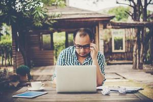 jovem empresário de óculos trabalhando no local de trabalho, sentindo-se estressado, olhando para o laptop foto