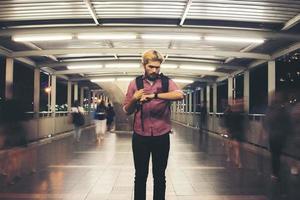 bonito homem barbudo parado na rua enquanto olha para smartwatch viajando à noite foto