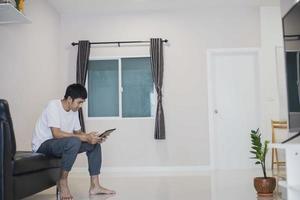 homem asiático segurando o tablet em casa no sofá foto