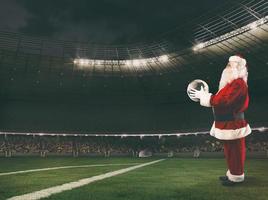 santa claus com uma futebol bola dentro dele mãos dentro uma futebol estádio foto