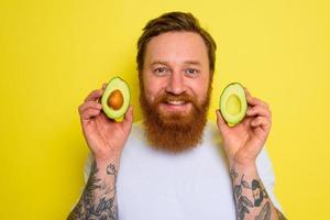 feliz homem com barba e tatuagens detém a abacate foto