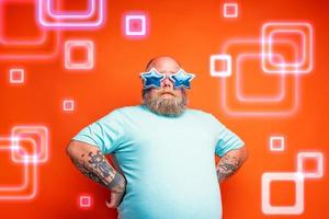 gordo pensativo homem com barba, tatuagens e oculos de sol é pronto para dança música foto
